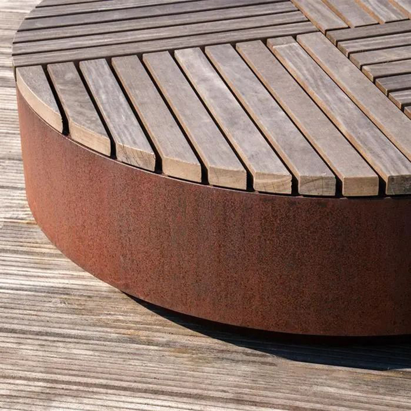 Détail d’un banc circulaire en acier Corten équipé d’une assise composée de lames de bois.