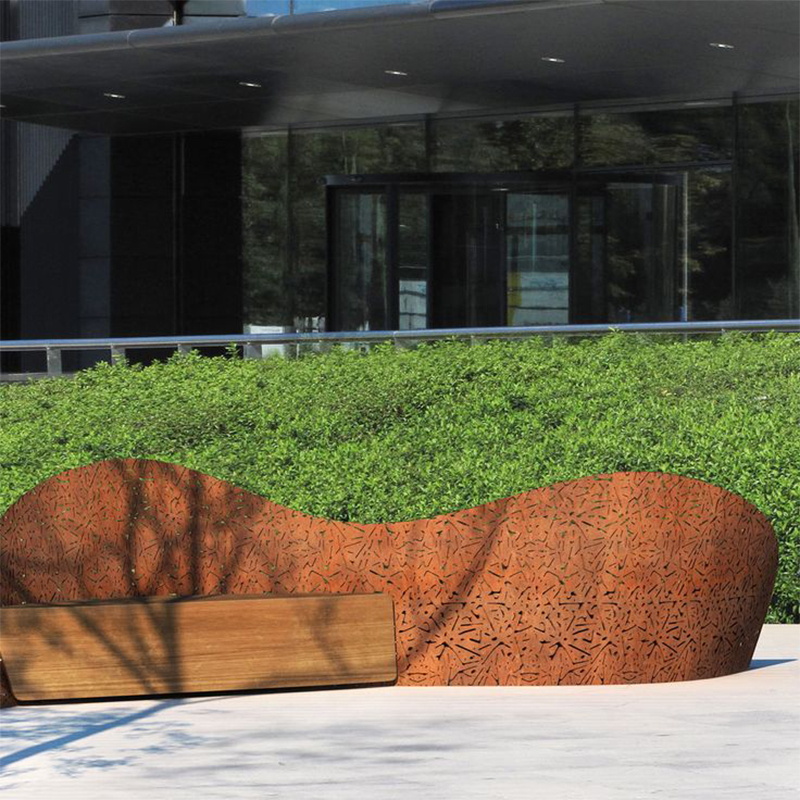 Banc urbain sculptural associant une structure courbe perforée en acier Corten et une assise rectangulaire en bois.