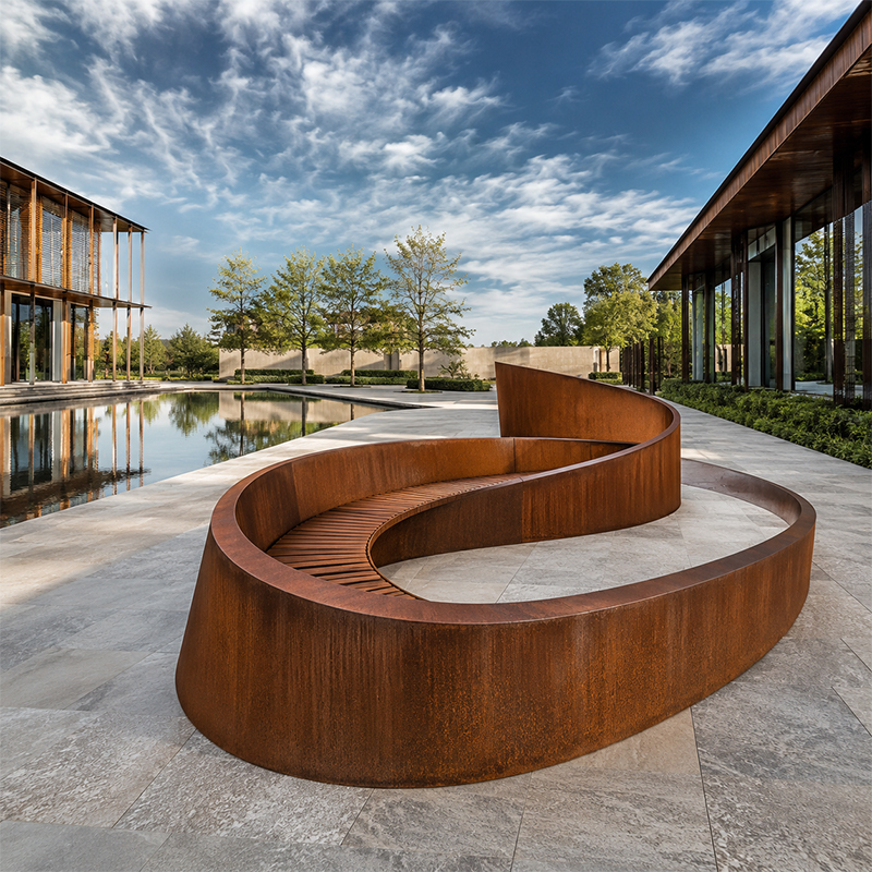Grande banquette architecturale aux formes courbes en acier Corten avec assise intégrée en bois dans un espace public contemporain.