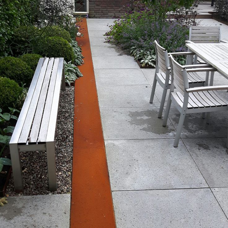 Longue bordure linéaire en acier Corten séparant une terrasse dallée d’un massif végétalisé dans un jardin résidentiel.