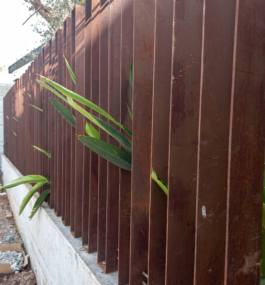 Claustra composé de lames verticales en acier Corten installé le long d’un jardin pour filtrer les regards.