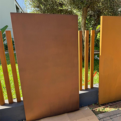 Claustra extérieur alternant grands panneaux pleins et fines lames verticales en acier Corten devant un jardin.