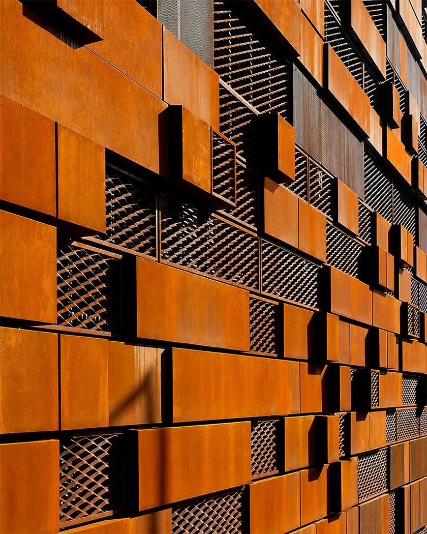 Façade contemporaine composée de panneaux en acier Corten disposés en relief et associés à des éléments métalliques ajourés.