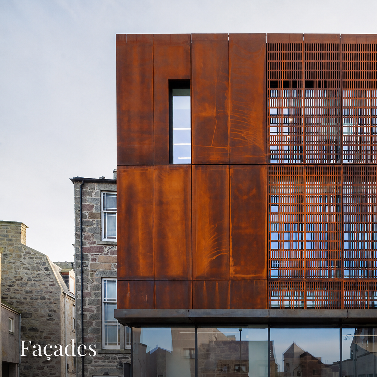 Façade contemporaine habillée de panneaux et de brise-soleil en acier Corten associés à une structure vitrée.