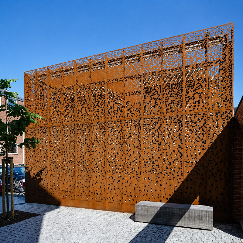 Façade monumentale composée de panneaux perforés en acier Corten formant une enveloppe ajourée devant un bâtiment public.
