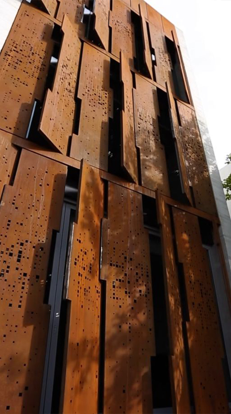 Façade contemporaine composée de panneaux perforés en acier Corten disposés en relief devant les ouvertures du bâtiment.