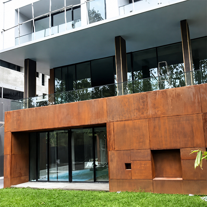 Façade inférieure d’une villa contemporaine habillée de grands panneaux rectangulaires en acier Corten autour des baies vitrées.