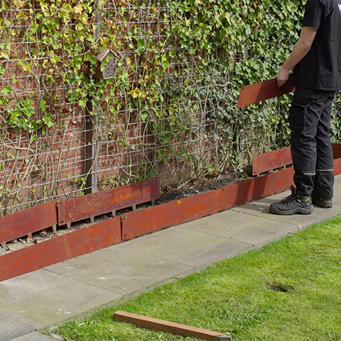 Technicien installant des éléments de bordure en acier Corten le long d’un aménagement paysager.