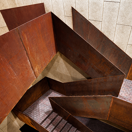 Escalier architectural sur mesure avec limons et garde-corps en acier Corten installé dans un bâtiment contemporain.