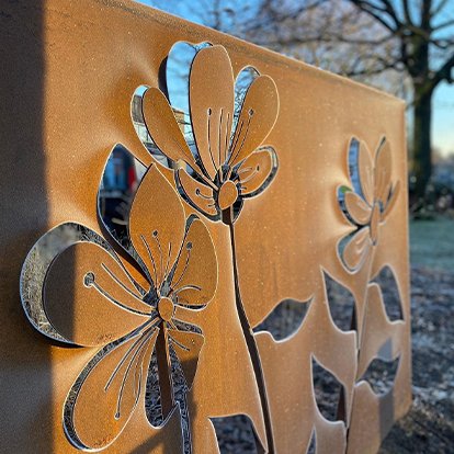 Gros plan d’un panneau décoratif en acier Corten présentant des fleurs découpées et des détails métalliques en relief.