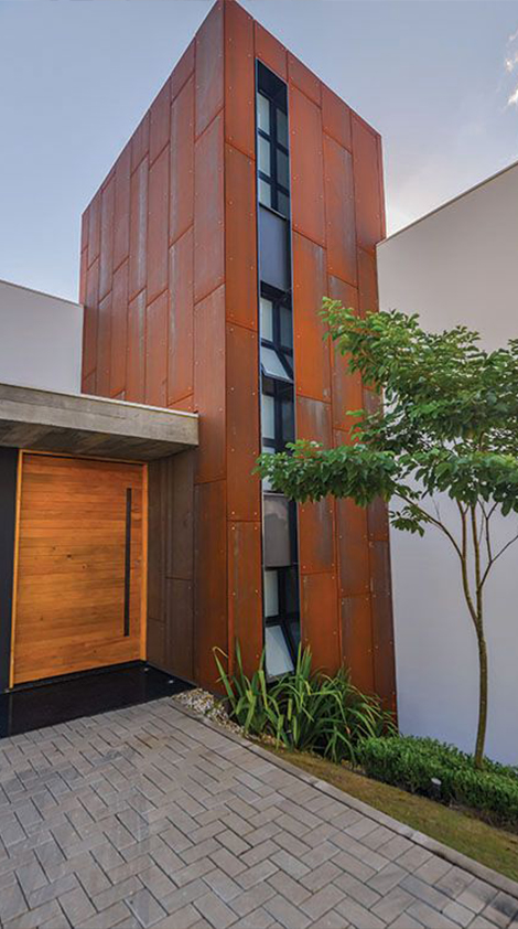 Tour d’entrée contemporaine recouverte de panneaux en acier Corten avec baie vitrée verticale et porte en bois